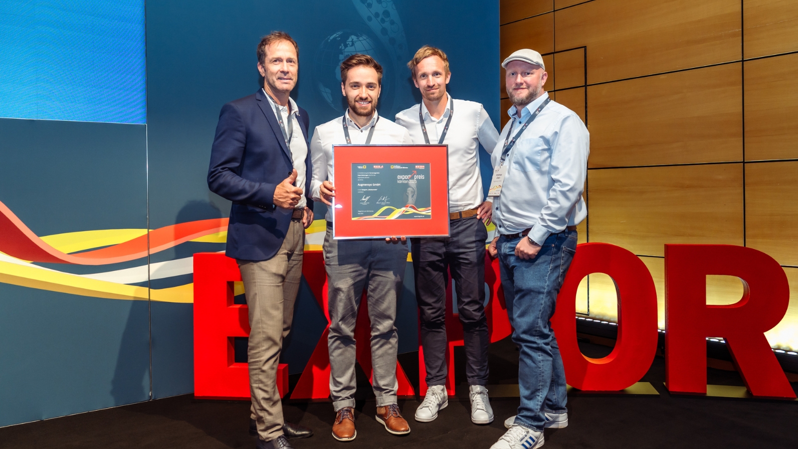 CEO und drei Teammitglieder von Augmensys auf der Bühne der Exportgala 2025 in Klagenfurt, halten die Nominierungsurkunde für den Kärntner Exportpreis in die Höhe.